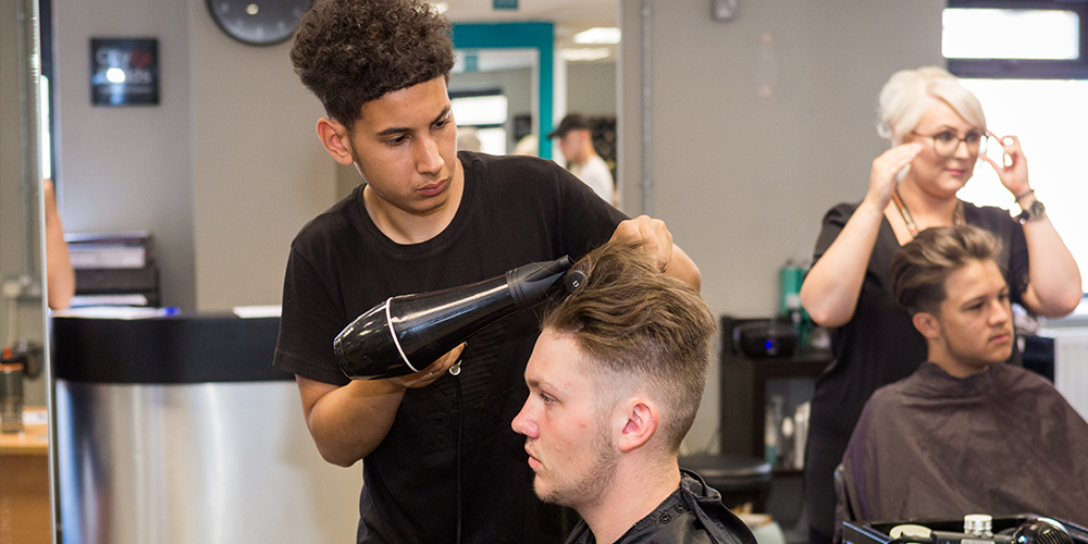 Barbering learner blow drying a man's hair