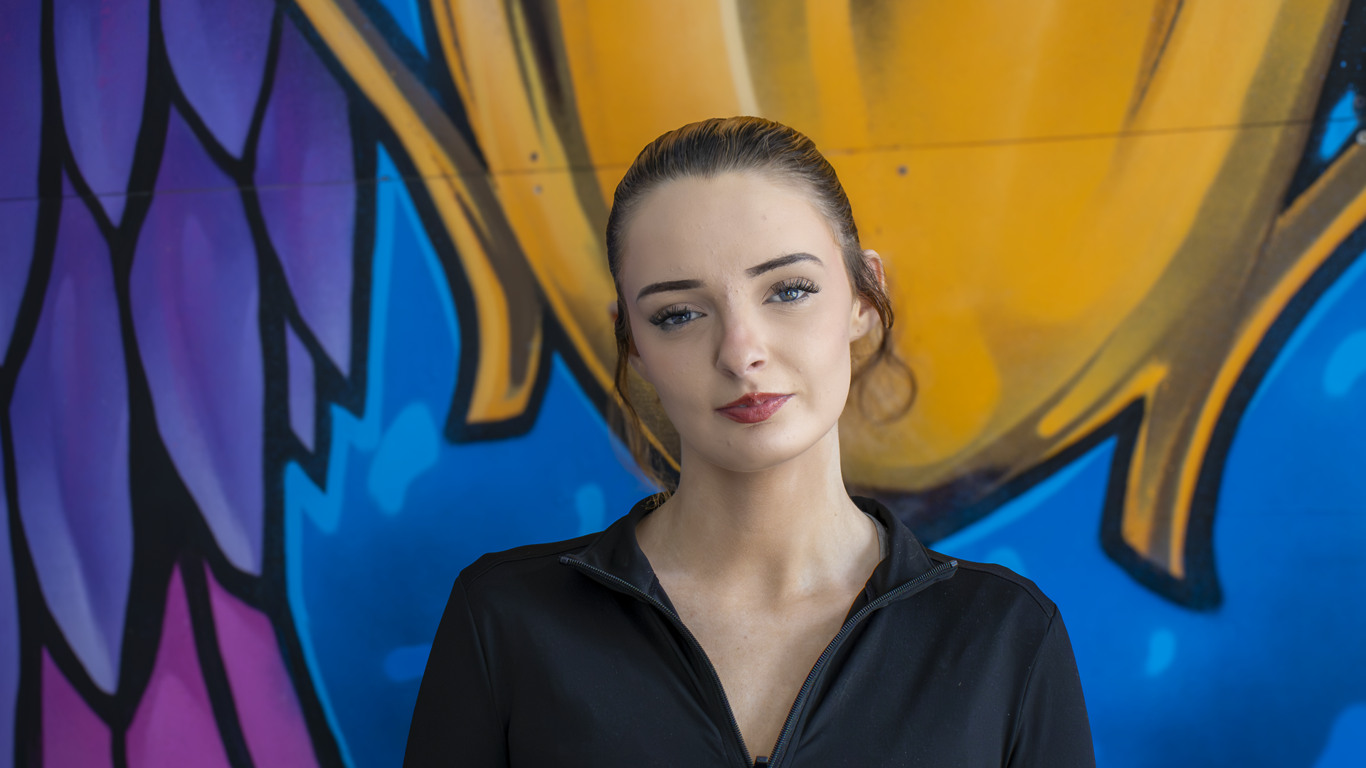 Learner Abby standing in front of a graffiti wall