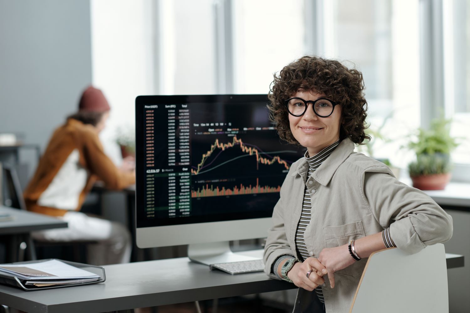 Woman sat at a desk, with a computer behind her.